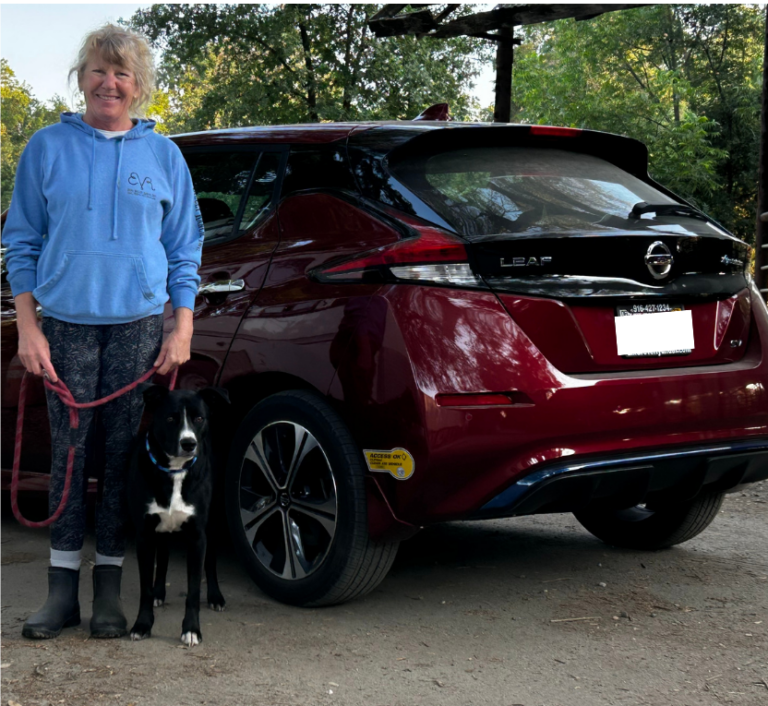 Woman and dog posing next to an electric car